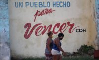 Cuban women walk past by a political slogan.