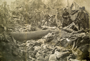 U.S. soldiers stand over a trench filled with Moro dead after the 1906 Bud Dajo massacre.
